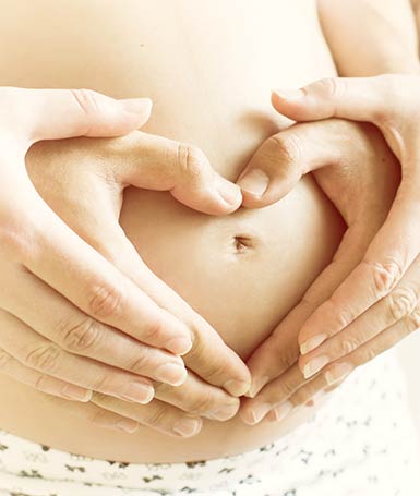 woman and man's hands form a heart shape over pregnant belly